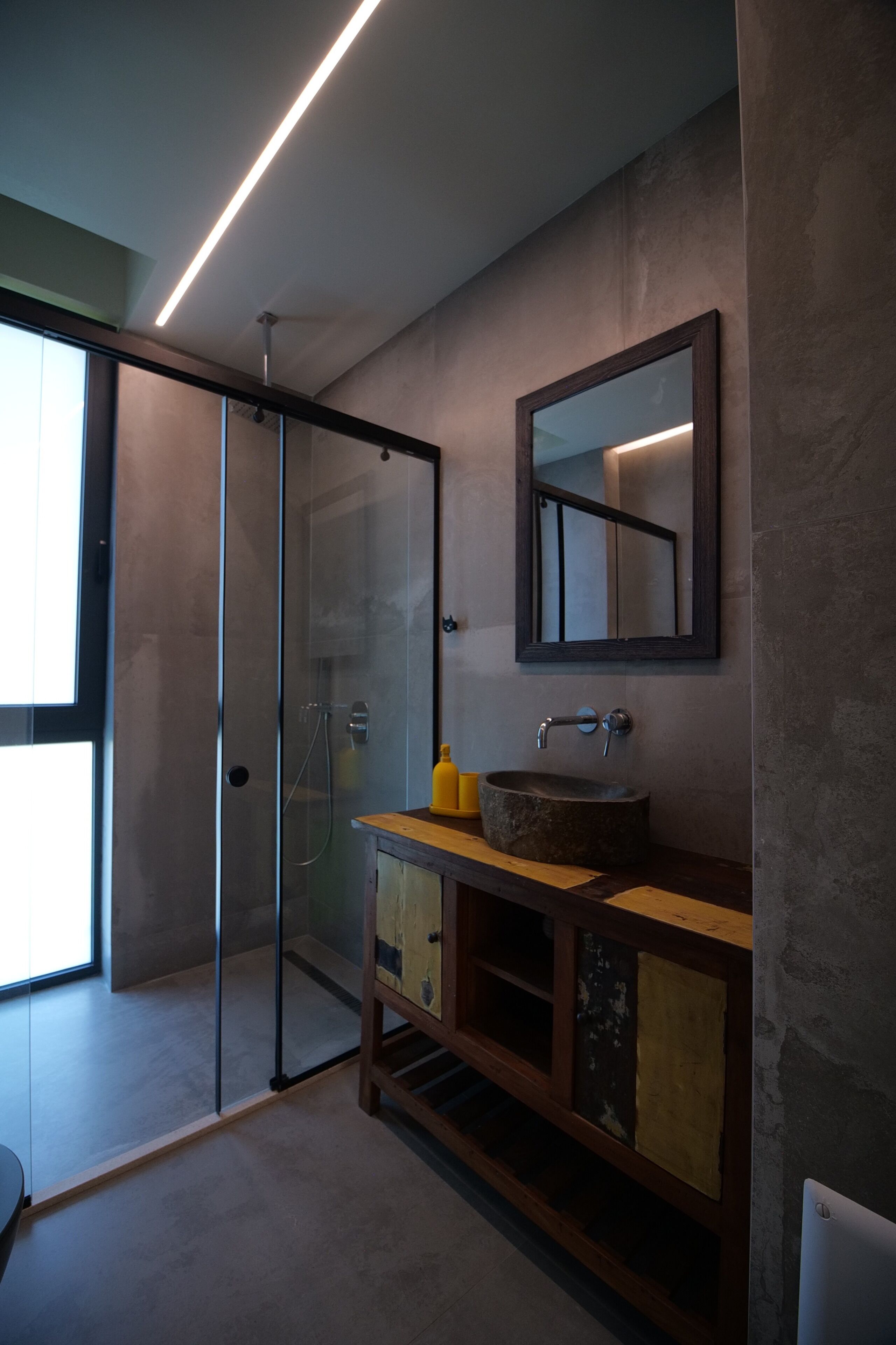 Une salle de bain moderne avec une douche à l’italienne en verre, un meuble-lavabo en bois avec un vasque en pierre et un grand miroir.