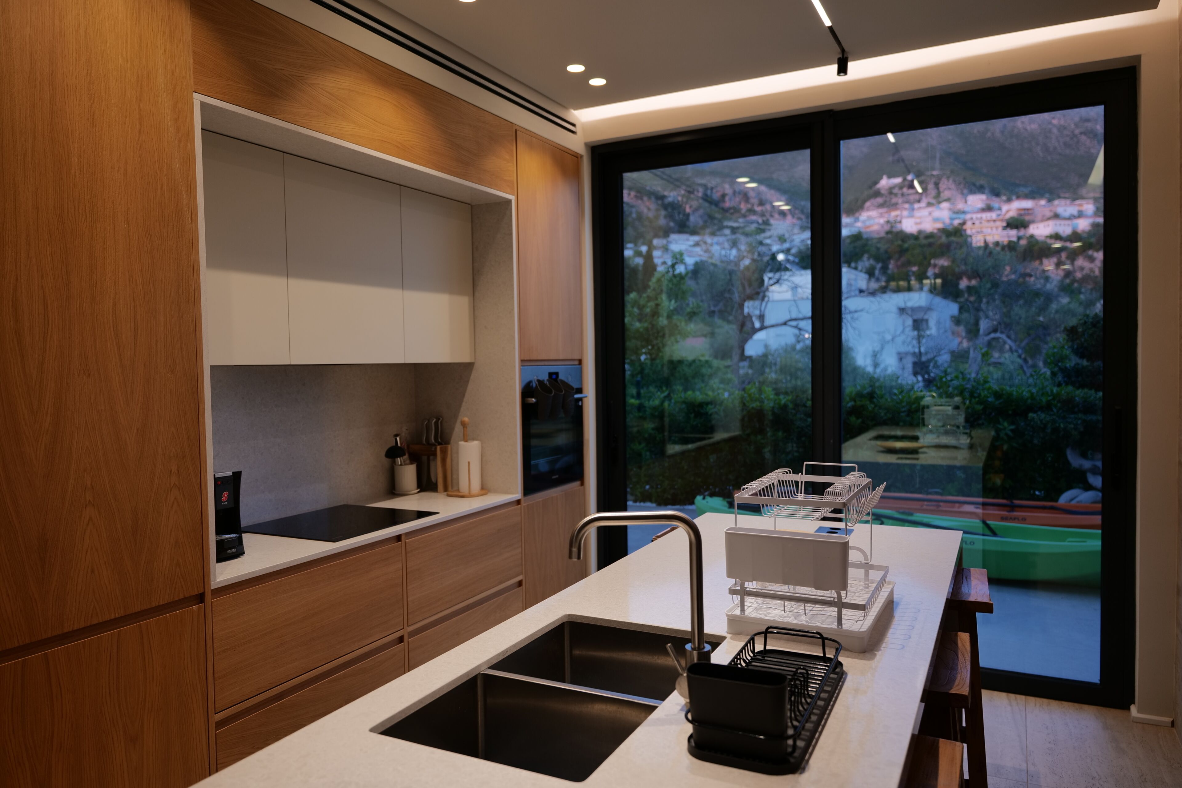 Una cocina moderna con un ventanal grande, armarios de madera y un lavamanos empotrado.