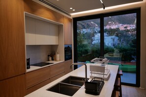 A modern kitchen with a large window, wooden cabinets, and a built-in sink. - Stay By Ilvesta Dhermi (Dhërmi)