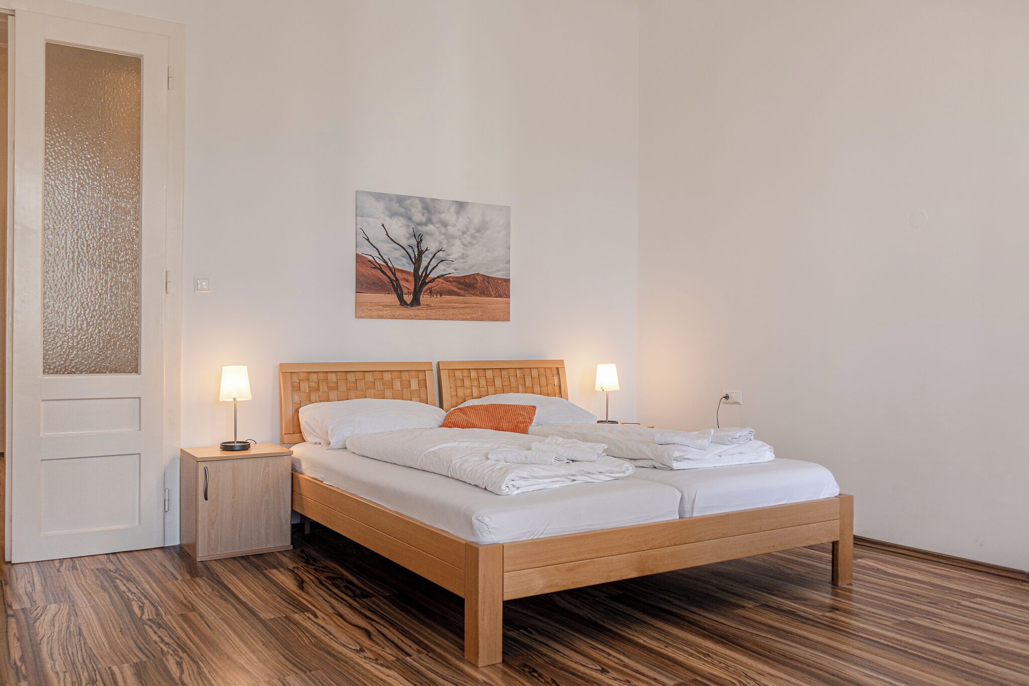 A neatly made bed with white linens, a wooden headboard, and two bedside lamps.