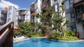 A modern hotel with a swimming pool surrounded by lush greenery and balconies with wooden railings. - Canvas 111/2 2-bedroom Residence (Choeng Thale)