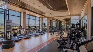 A modern gym with treadmills, elliptical machines, and weight equipment. Large windows offer views of the outdoors. - Canvas 111/2 2-bedroom Residence (Choeng Thale)