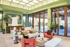 Un espacio interior amplio con techo alto, ventanas grandes y una disposición de asientos que incluye un sofá y sillones.
