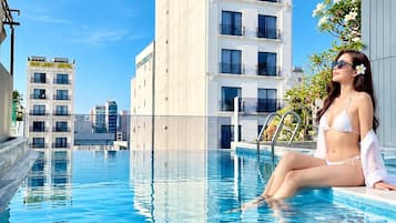 Una piscina con una persona sentada en el borde, rodeada de edificios modernos.