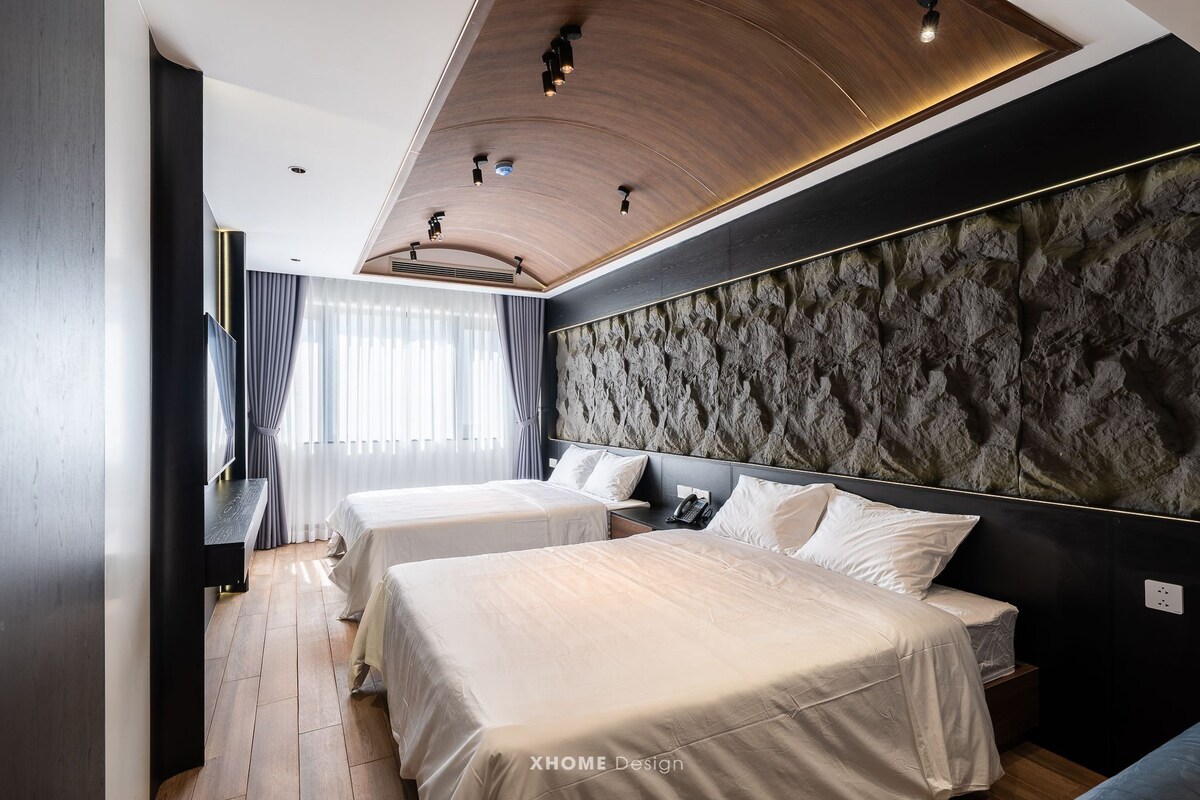 Una habitación de hotel moderna con dos camas, un ventanal con cortinas, un muro texturizado e iluminación empotrada en el techo.