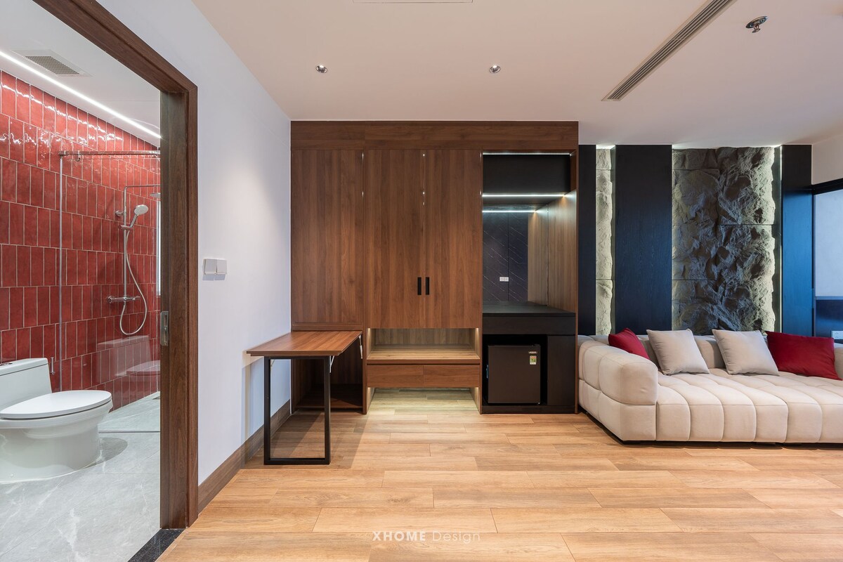 A modern bathroom with a shower, toilet, and vanity. There is a wooden bench and a sofa with cushions.