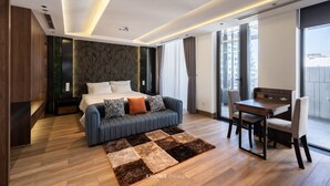A modern hotel room with a bed, a sofa, a dining table, and a view of the city. - La Anima Hotel & Apartment (Da Nang)