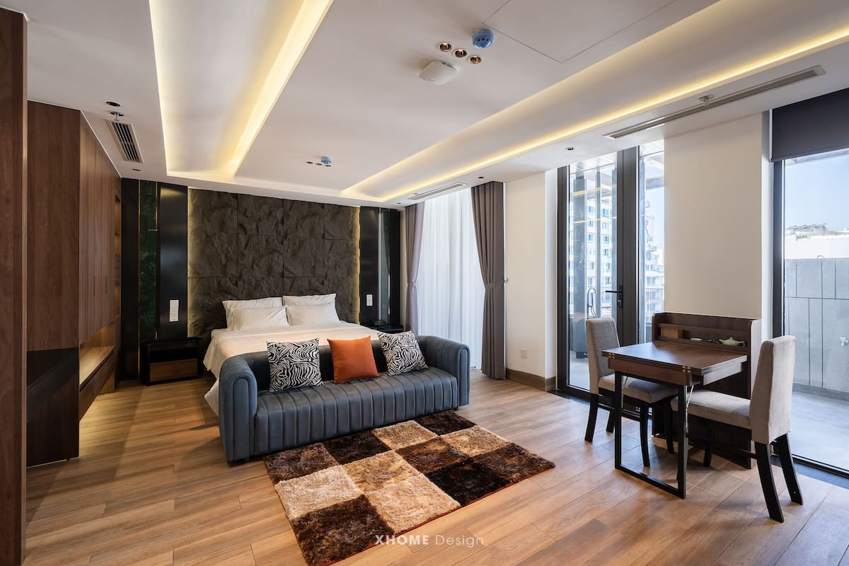 Habitación de hotel moderna con cama, sofá, mesa de comedor y vista a la ciudad.