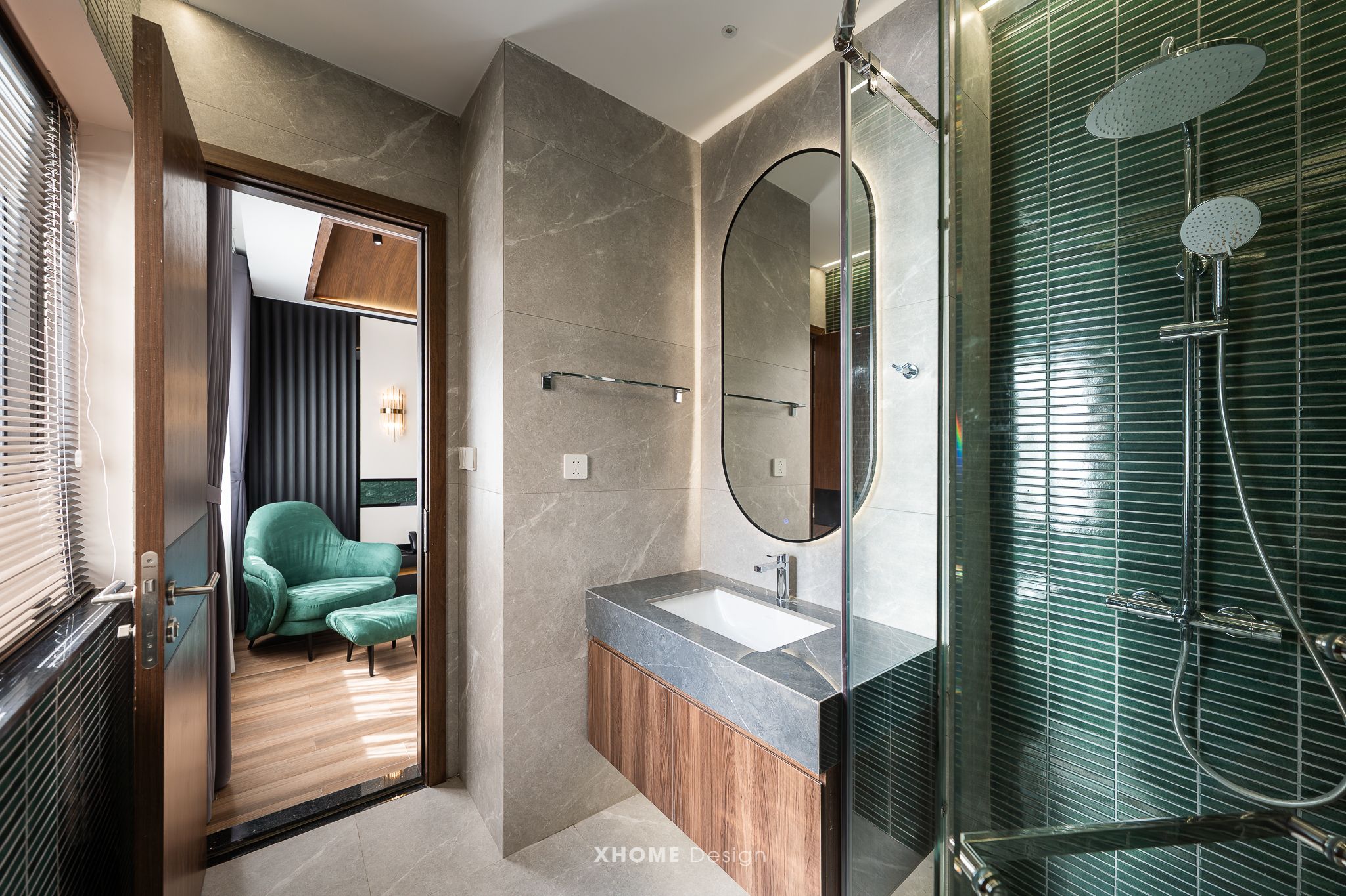 A modern bathroom with a glass shower enclosure, a vanity with a marble countertop, and a green upholstered chair in the adjacent room.