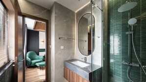 A modern bathroom with a glass shower enclosure, a vanity with a marble countertop, and a green upholstered chair in the adjacent room. - La Anima Hotel & Apartment (Da Nang)