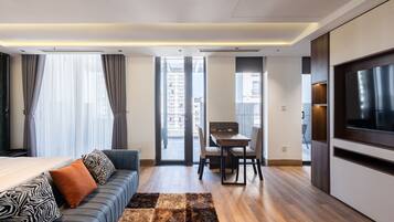 A modern hotel room with a sofa, a dining table, and a TV.
