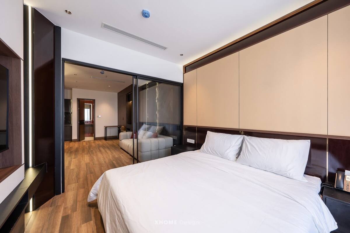 Una habitación de hotel moderna con una cama grande, un sofá y un separador de vidrio que divide la sala de estar del dormitorio.