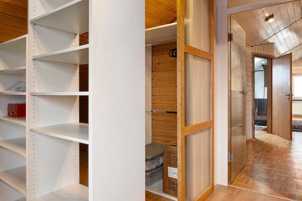 A room with white shelving units, a wooden floor, and a door leading to another room.