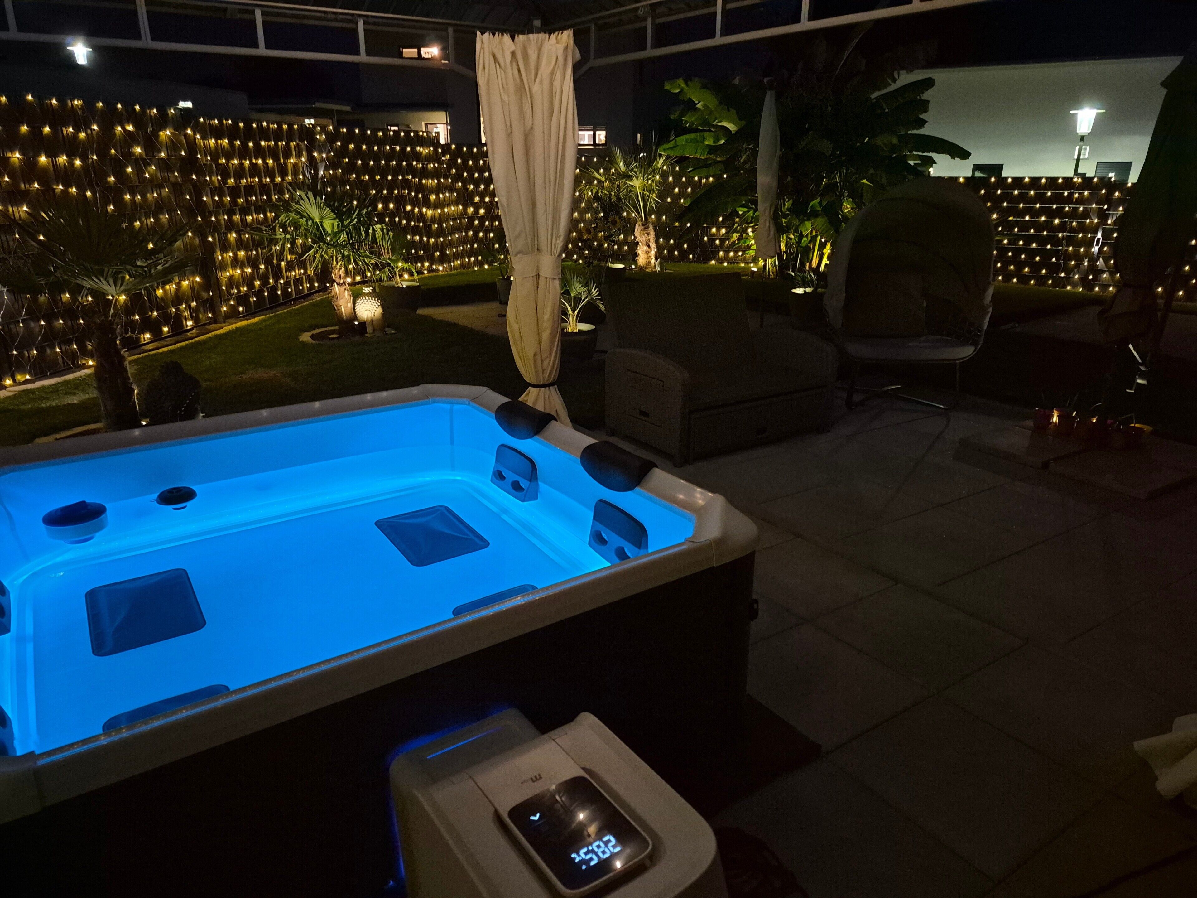 Ein Whirlpool mit digitaler Anzeige, umgeben von Außenmöbeln und einer dekorativen Lichtwand.
