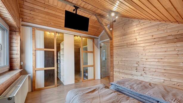 A wooden-paneled room with a bed, a sliding glass door leading to a bathroom, and a mounted television. - Apartment 'Witt' with Whirlpool, Palm Garden, and Terrace (Salem)