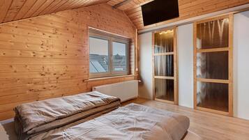 Una habitación con paneles de madera, una cama, un ventanal, un radiador y un televisor montado en el techo.