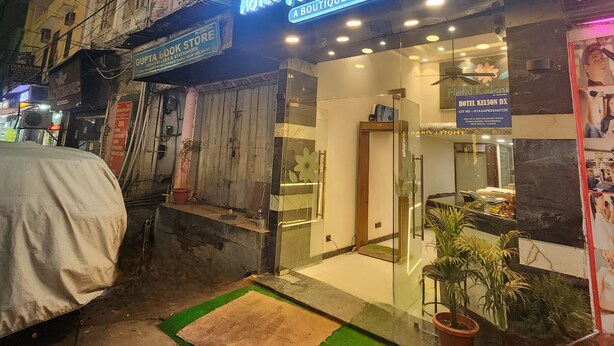 Hotel Kelson DX with a modern facade, a visible entrance, and a small outdoor seating area with a green mat and potted plants. - Hotel Kelson DX-Near Ramakrishna Metro (New Delhi)