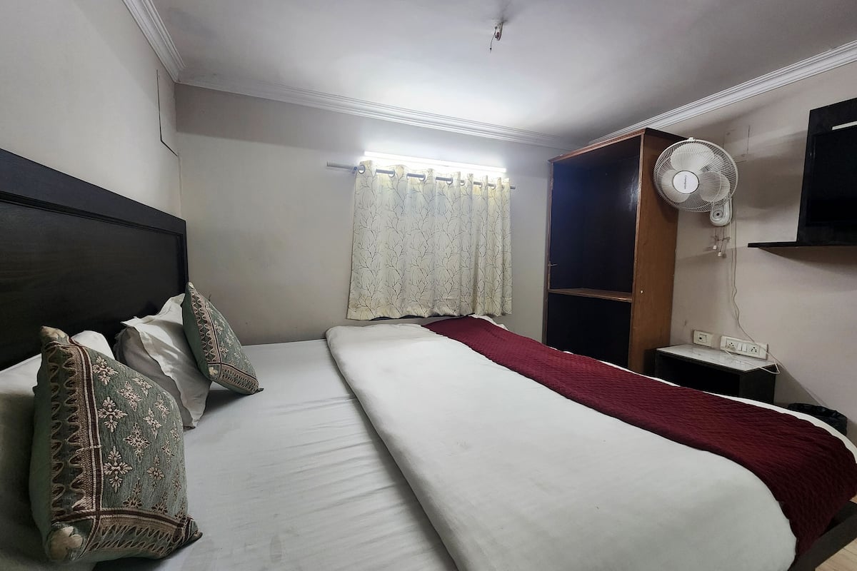 Ein Hotelzimmer mit Bett, Nachttisch, Wandventilator und Fernseher.