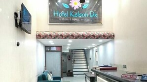 A hotel reception area with a modern design, including a reception desk, a sofa, a ceiling fan, and a staircase in the background. - Hotel Kelson DX-Near Ramakrishna Metro (New Delhi)