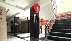 A modern interior with a marble floor, a red fire alarm, and a staircase with black steps. - Hotel Kelson DX-Near Ramakrishna Metro (New Delhi)