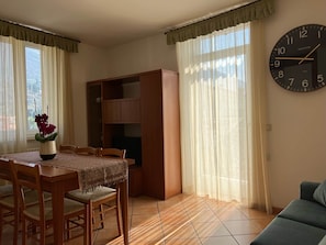 A dining area with a wooden table and chairs, a bookshelf, and a large wall clock. - Superior 5 (Nago-Torbole)