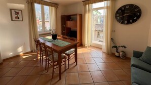Een eetgedeelte met een houten tafel en stoelen, een klok aan de muur en uitzicht door het raam.