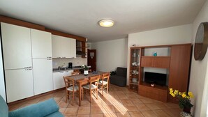A compact living space with a kitchen, dining area, and a seating area with a sofa and TV stand. - Family Baia 6 (Nago-Torbole)