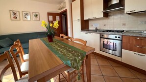 A compact kitchen with a dining area, featuring a wooden table, chairs, a stove, oven, and cabinets. - Family Baia 6 (Nago-Torbole)