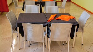 Un área de comedor con mesas y sillas, una planta y una cortina roja.