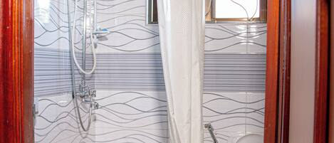 A bathroom with a shower, toilet, and sink, featuring a patterned tile wall and a wooden door frame.