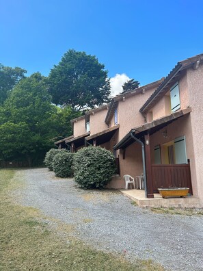 Un bâtiment à deux étages avec une allée gravillonnée, une clôture en bois et un grand arbre en arrière-plan.