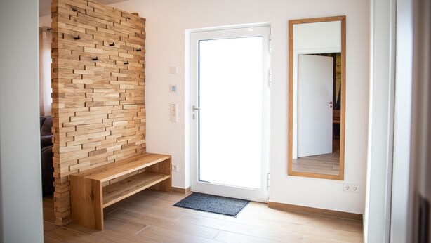 A hallway with a wooden wall, a bench, a door, and a mirror.
