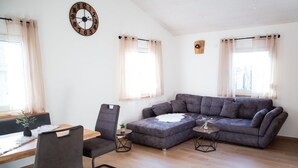 A living room with a sofa, chairs, a table, and a clock on the wall.