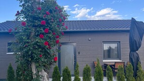 A modern house with a garden, a tree with red flowers, and a covered outdoor seating area.