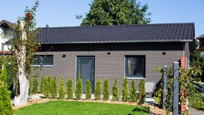 A modern house with a grey exterior, a tiled roof, and a well-maintained garden with young trees and a lawn.