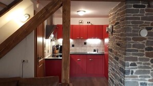 Une cuisine avec des meubles de couleur rouge, un escalier en bois et un mur en pierre.