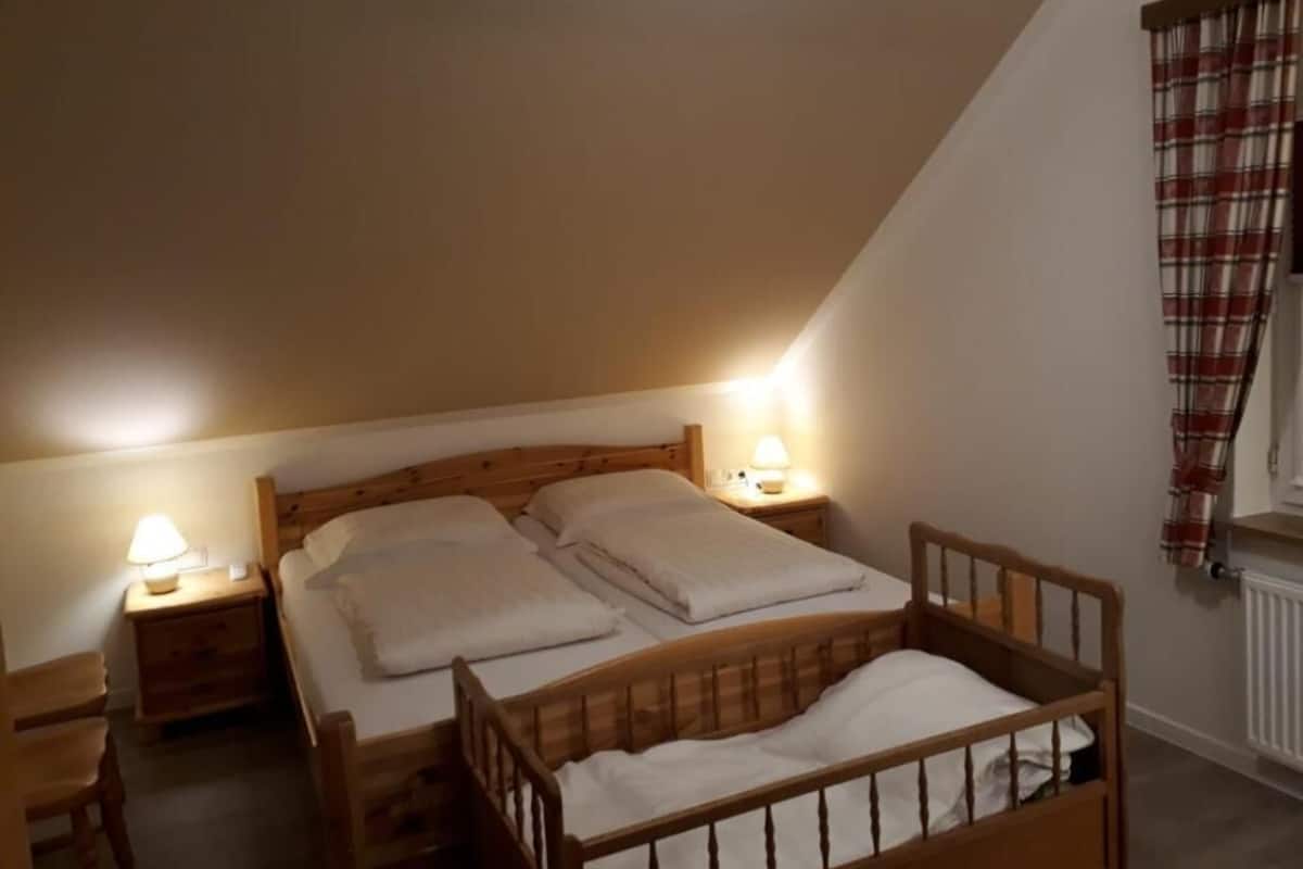Ein gemütliches Schlafzimmer mit schrägen Wänden, zwei Betten, Holz-Kopfteilen und Nachttischlampen.