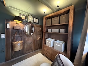 Ein Zimmer mit Holztür, Spiegel, Briefschlitz, Korb und Stauraum mit Kisten.