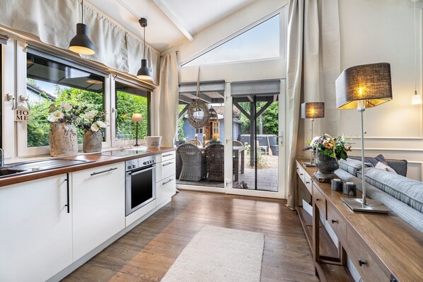 Une cuisine moderne dotée d’une grande fenêtre, un coin repas avec des meubles en osier et un espace salon confortable avec un canapé et une lampe.