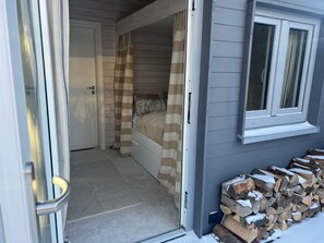 Un dormitorio con cama, ventana y puerta. Hay una pila de leña afuera.