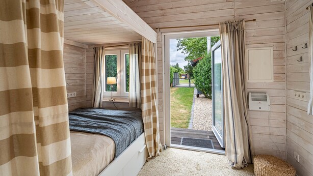 Une pièce avec un lit, des rideaux, une fenêtre, une porte et une vue sur l’extérieur.