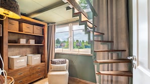 Une pièce avec un escalier en bois, une fenêtre donnant sur un paysage agréable, une chaise et un meuble de rangement avec des boîtes.