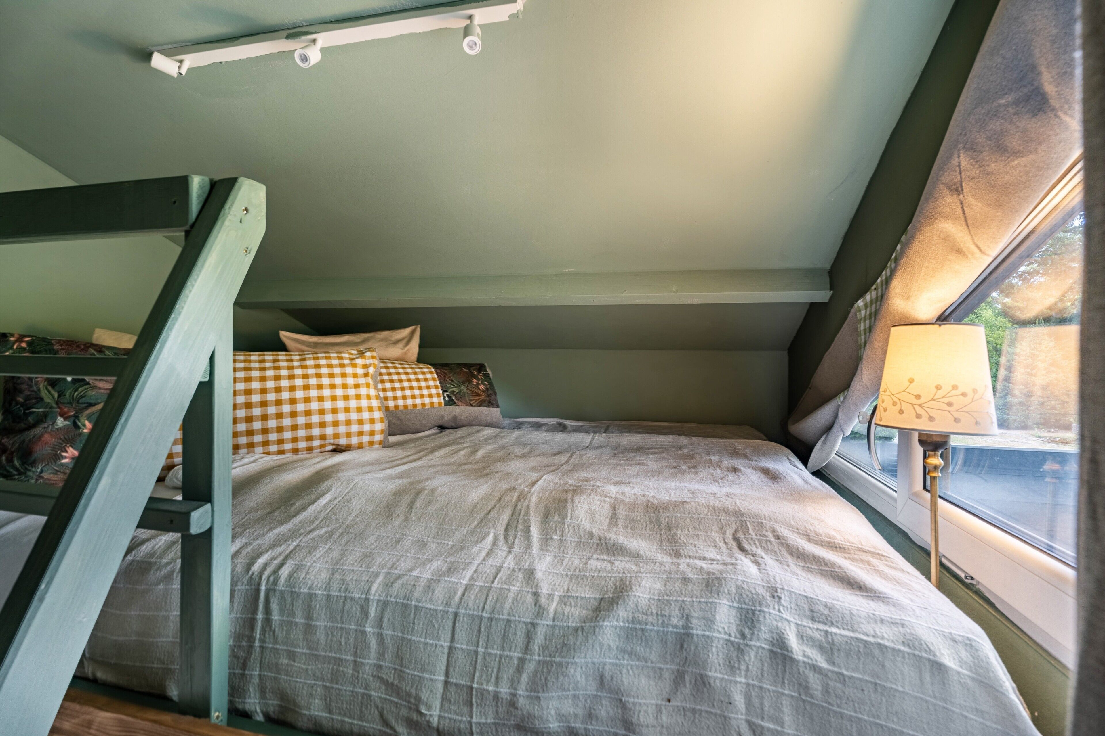 A bunk bed with a checkered pillow, a bedside lamp, and a window with curtains.