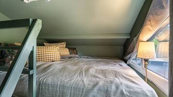 A bunk bed with a checkered pillow, a bedside lamp, and a window with curtains.