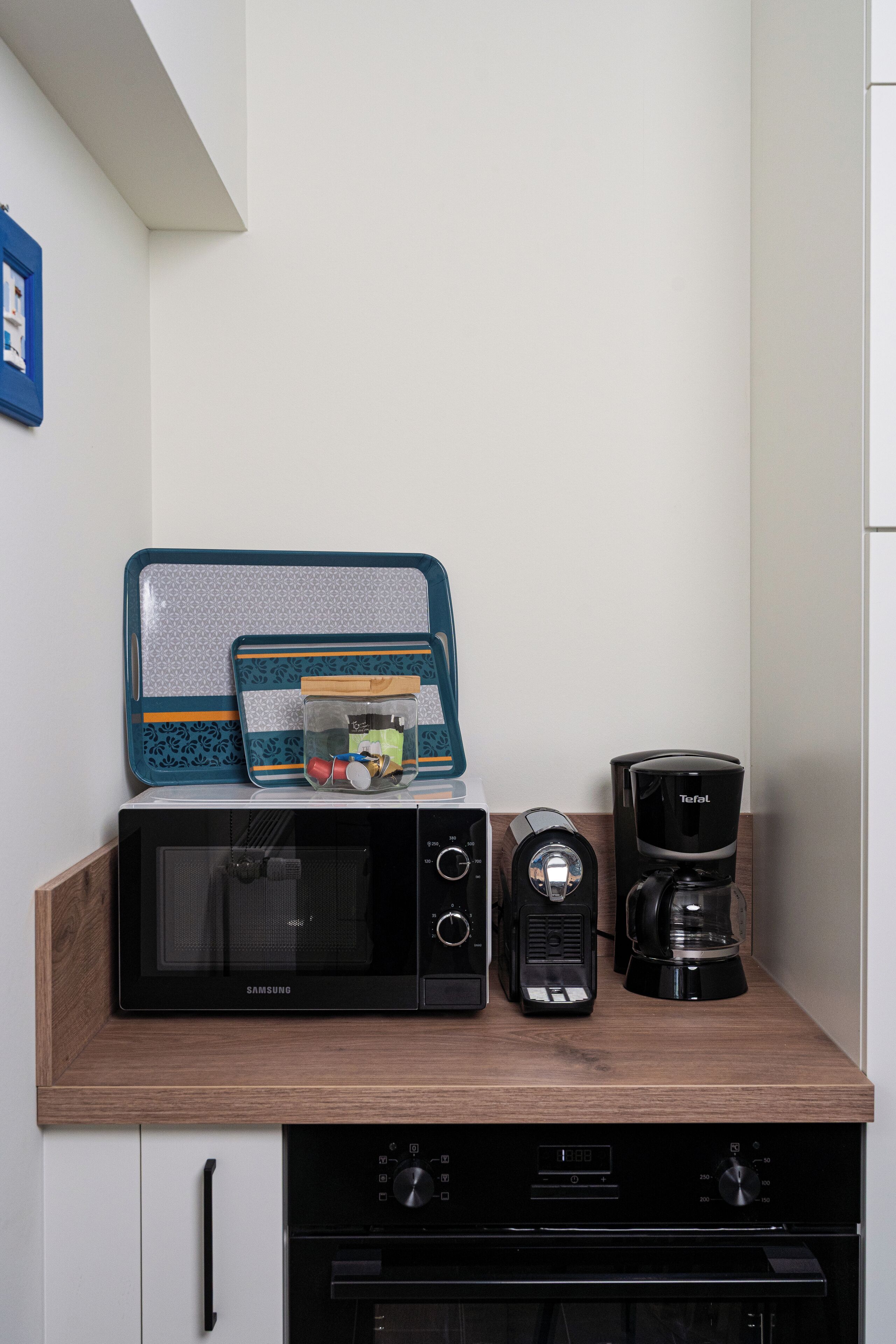 Cucina con forno a microonde, macchina del caffè e contenitori portaoggetti su un piano di lavoro in legno.