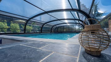 Une piscine intérieure dotée d’un plafond en verre transparent, d’un sol en pierre et d’un panier en osier placé à droite.