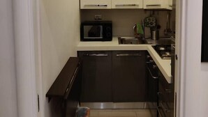Een kleine keuken met witte kastjes, een magnetron, een spoelbak en een vaatwasser.