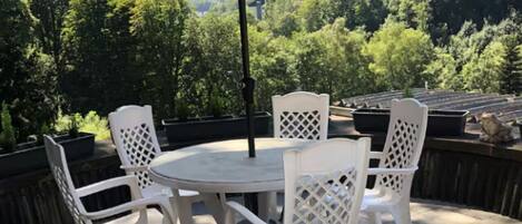 A patio with a round table and four chairs, an umbrella, and a view of a forested hillside.