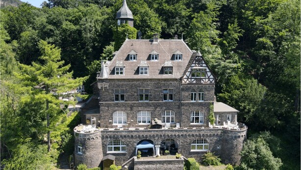 Ein großes, historisches Steinhaus mit vielen Fenstern und einem Turm, umgeben von üppigem Grün.
