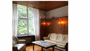 Ein Zimmer mit Holzboden, einer Couch, einem Sessel, einem Tisch und einem Fenster mit Vorhängen.